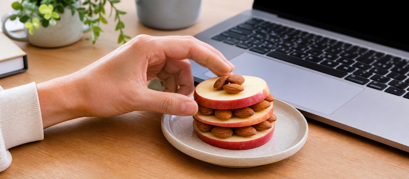 Hand reaching for an almond-and-apple snack stack next to a laptop keyboard